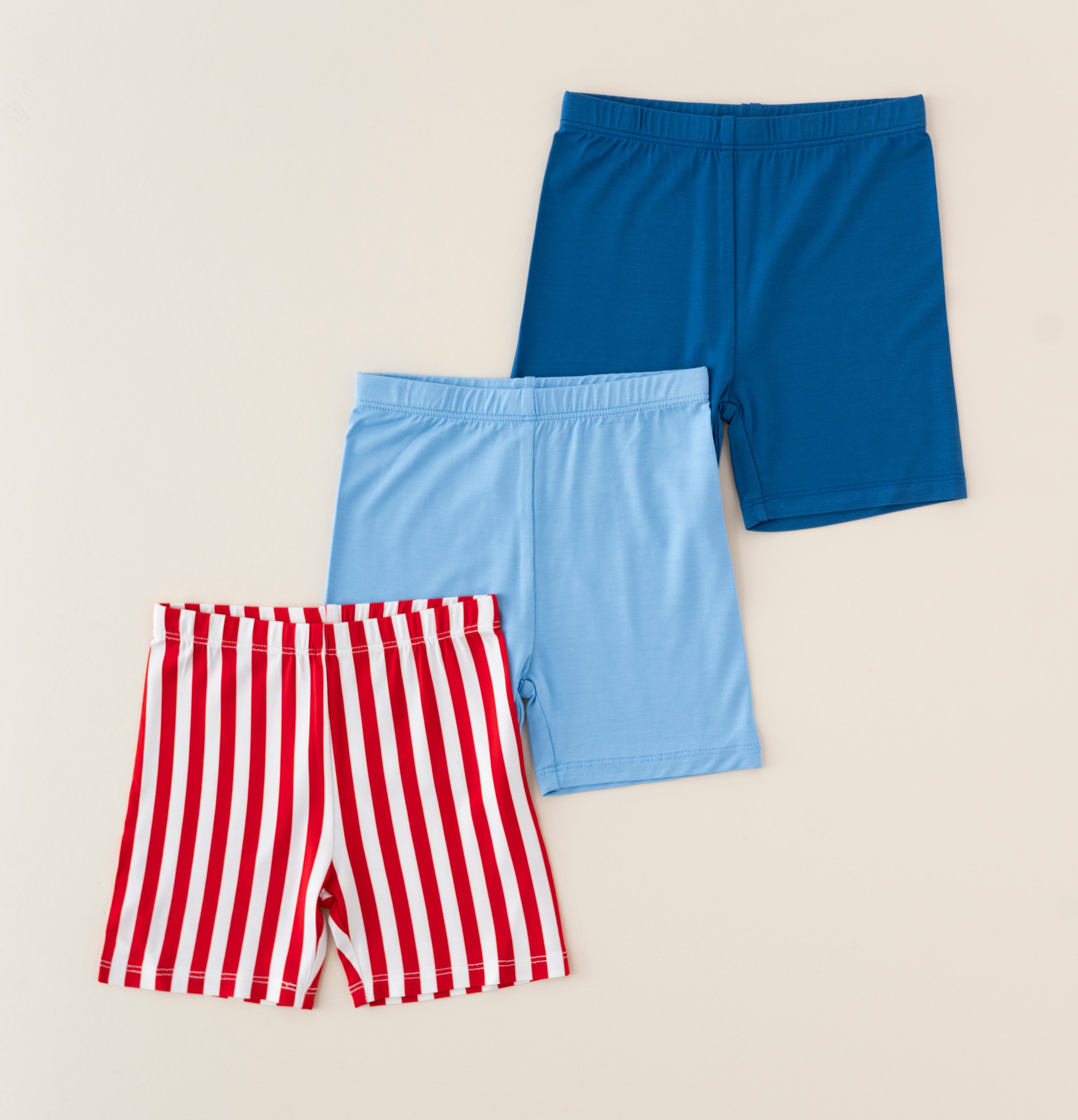 Three pairs of bamboo biker shorts in blue, red and white stripes, and cobalt blue on a beige background